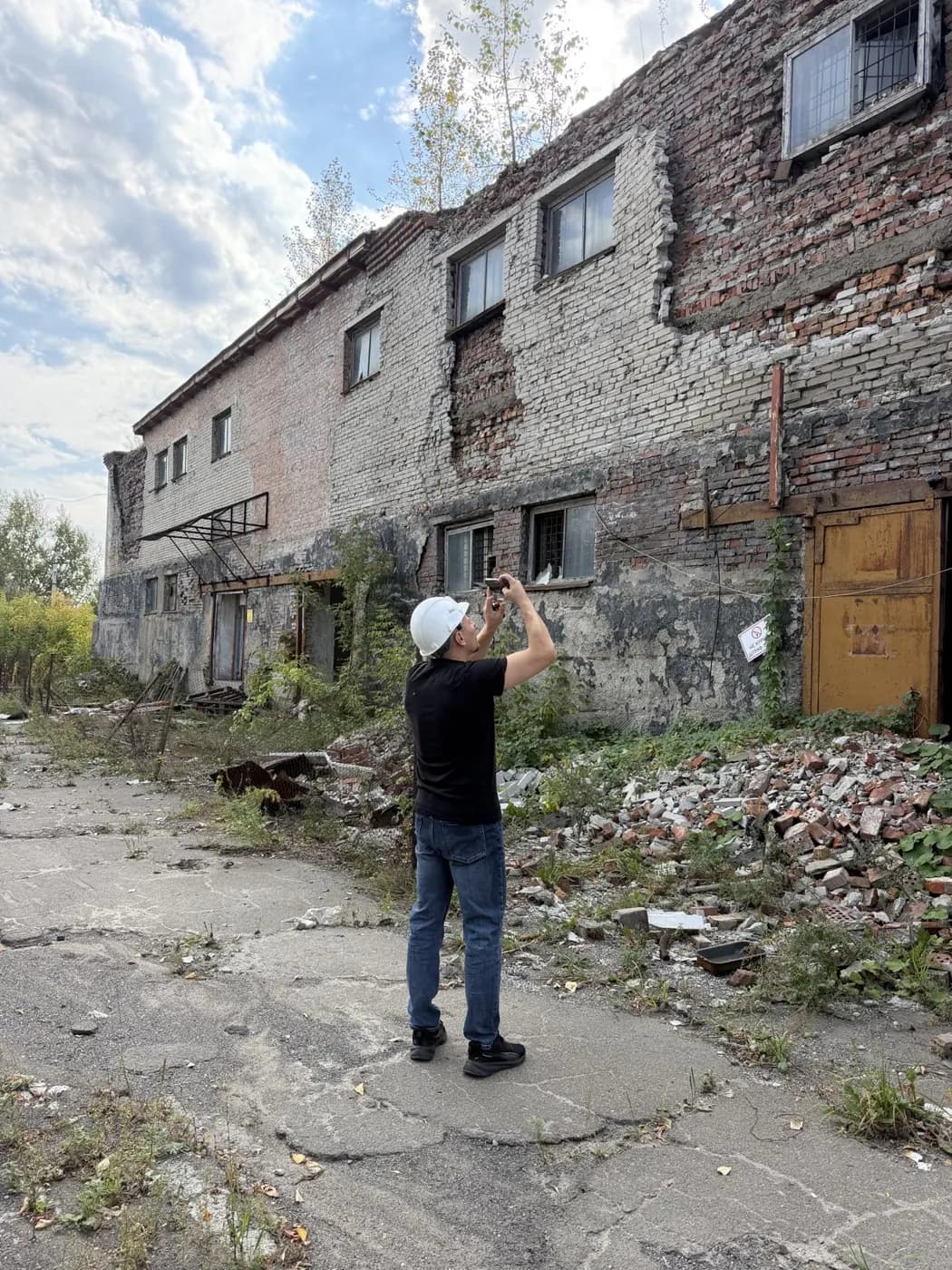 Инженер НЭА в каске фотографирует фасад производственного здания при обследовании